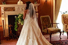An elegant bride stands in one of the elegant living areas of the Frank Phillips Mansion, in front of the fireplace