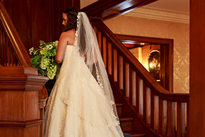 A beautiful bride stands on the stairs inside the Frank Phillips Mansion, the train of her dress cascades elegantly down the steps