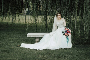 A beautiful bride sits on a stone bench under a willow tree in the Frank Phillips Mansion lawn